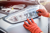 Mechanic holding lamp and cables from headlamp of car
