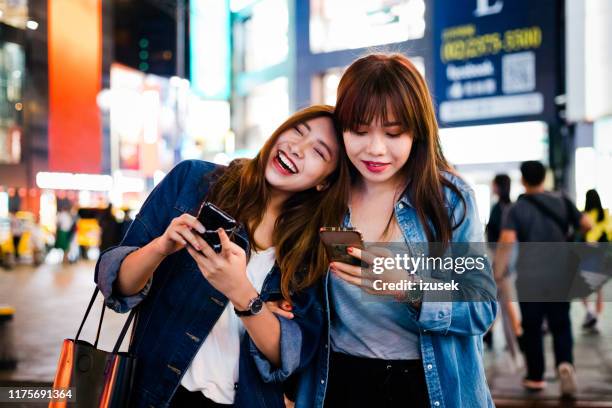 vrolijke vriendinnen die smart phone gebruiken in de stad - taiwanese etniciteit stockfoto's en -beelden