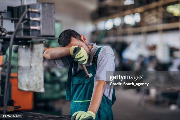 un tipo cansado trabajando en una máquina en el taller de la fábrica - sudor fotografías e imágenes de stock