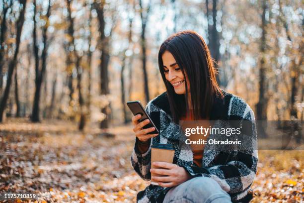 mujer feliz usando el teléfono inteligente en el hermoso día de otoño en el bosque - november fotografías e imágenes de stock