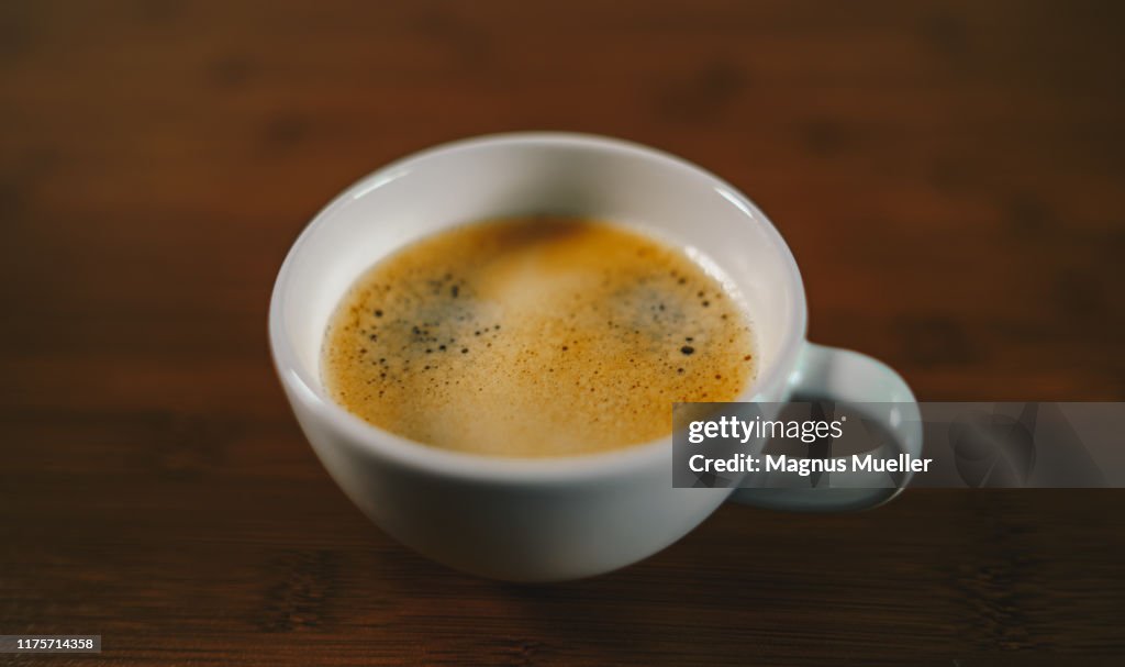 A white cup of black coffee on a wooden table