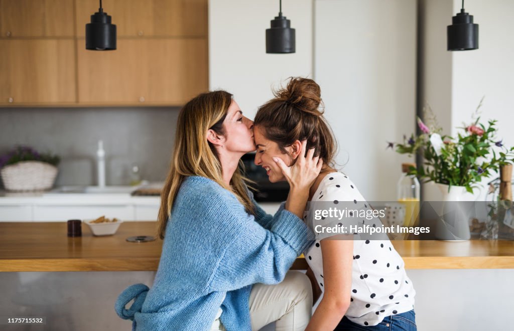 Front view portrait of mature mother with adult daughter sitting at home, kissing forehead.
