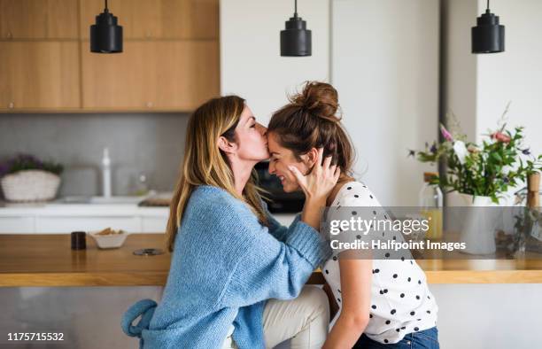 front view portrait of mature mother with adult daughter sitting at home, kissing forehead. - mum daughter stock pictures, royalty-free photos & images