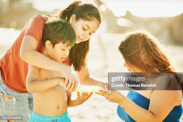 aunts helping young boy play with bubbles during family beach party - nephew stock-fotos und bilder