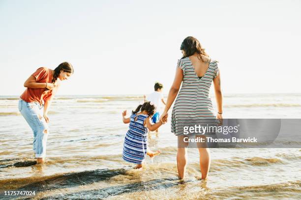 young girl playing in water at beach while holding mothers hand - tia imagens e fotografias de stock