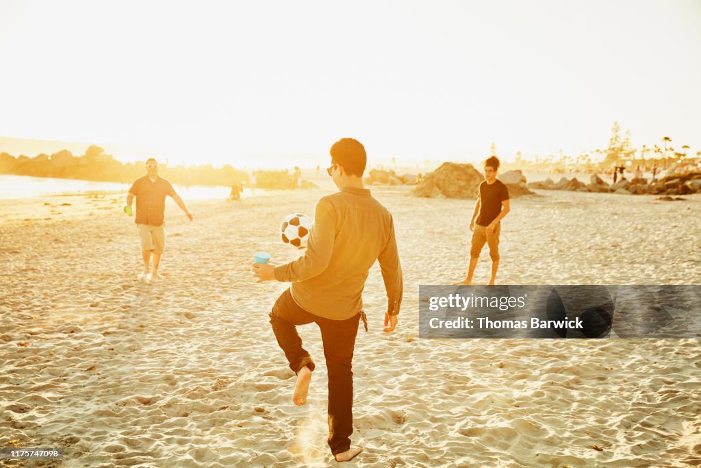 Man juggling soccer ball while playing with friends on beach