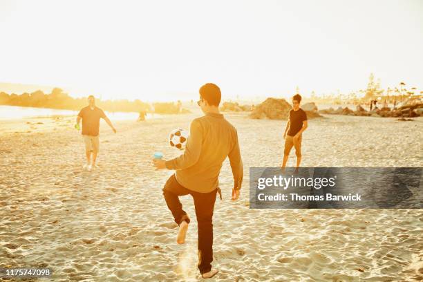 man juggling soccer ball while playing with friends on beach - kick ups stock pictures, royalty-free photos & images