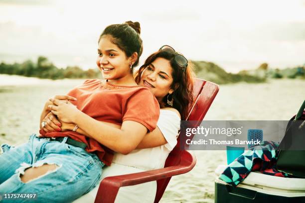 smiling daughter sitting on mothers lap during family beach party - us girls on the beach stock-fotos und bilder