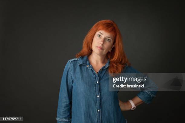 studio portrait of a 50 year old attractive red-haired woman in a blue dress on a black background - angry woman red stock pictures, royalty-free photos & images