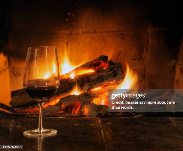 a crystal glass with red wine besides a burning fire of a fireplace. still life - log fire stock pictures, royalty-free photos & images