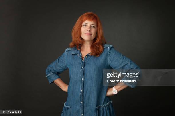 studioporträt einer 50-jährigen attraktiven rothaarigen frau in einem blauen kleid auf schwarzem hintergrund - 50 year old black woman stock-fotos und bilder