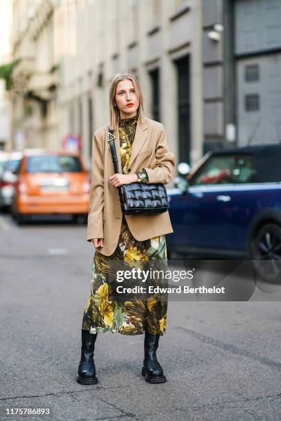 Guest wears a light brown blazer jacket, a black leather quilted bag, a green khaki and yellow floral print dress, black leather boots, outside the...