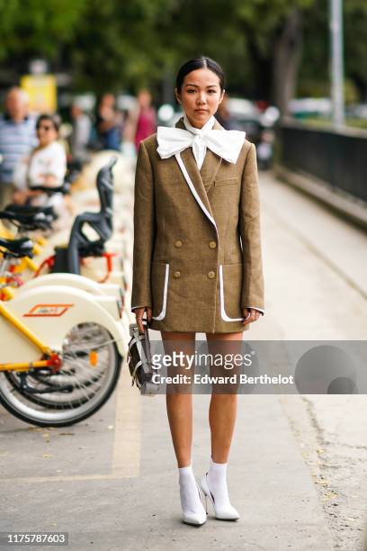 Yoyo Cao wears a brown blazer jacket dress, a white scarf, white high heeled shoes, a bag, outside the Fendi show during Milan Fashion Week...
