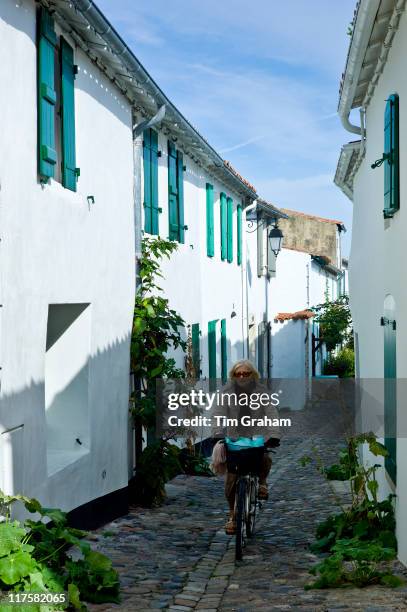 Traditional street scene woman cycles along cobbled alleyway at St Martin de Re, Ile de Re, France