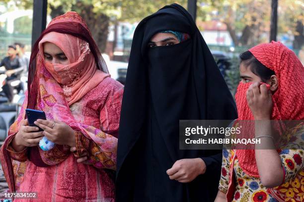 Women look on as they use mobiles phones in Srinagar on October 14 following Indian government's decision to restore mobile phones network in...