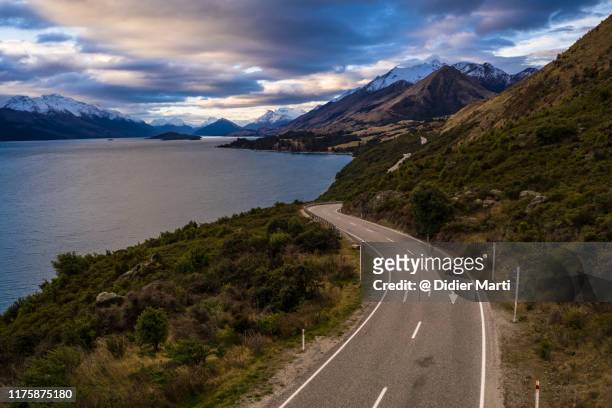 dramatic sunset over the road along lake wakapitu between queenstown and glenorchy in new zealand - arrows landscapes stock pictures, royalty-free photos & images