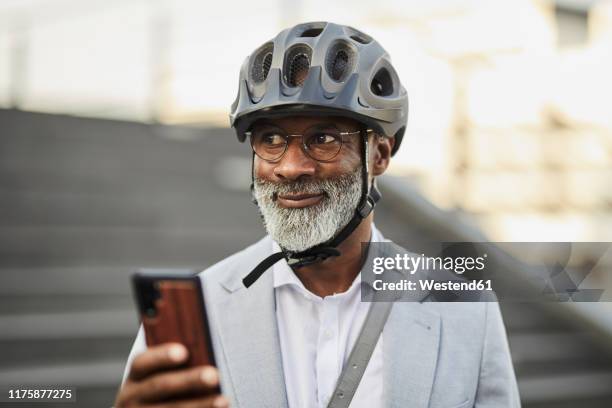 portrait of smiling mature businessman with smartphone wearing cycling helmet and glasses - cycling helmet stock pictures, royalty-free photos & images