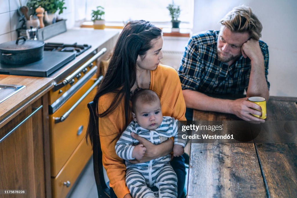 Serious family with baby sitting at kitchen table at home