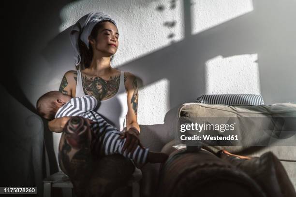 tattooed young woman holding her baby at home enjoying the sunshine - hot babe stock pictures, royalty-free photos & images