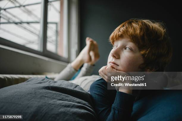 portrait of redheaded boy lying on couch out of window - junge träumt stock-fotos und bilder