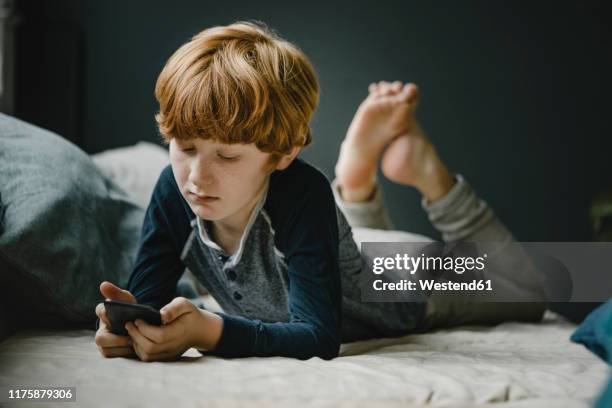 portrait of redheaded boy lying on couch looking at mobile phone - sad boy stock-fotos und bilder