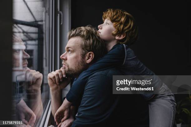 father and son looking out of window on rainy day - niños pensando fotografías e imágenes de stock