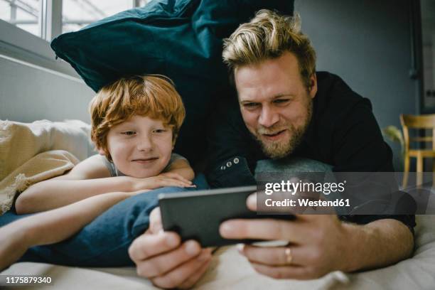 portrait of father and son lying on couch looking at cell phone - child mobile phone stock-fotos und bilder