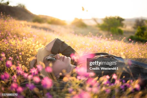 young woman with sunhat lying on meadow at sunset - frau blumenwiese stock-fotos und bilder