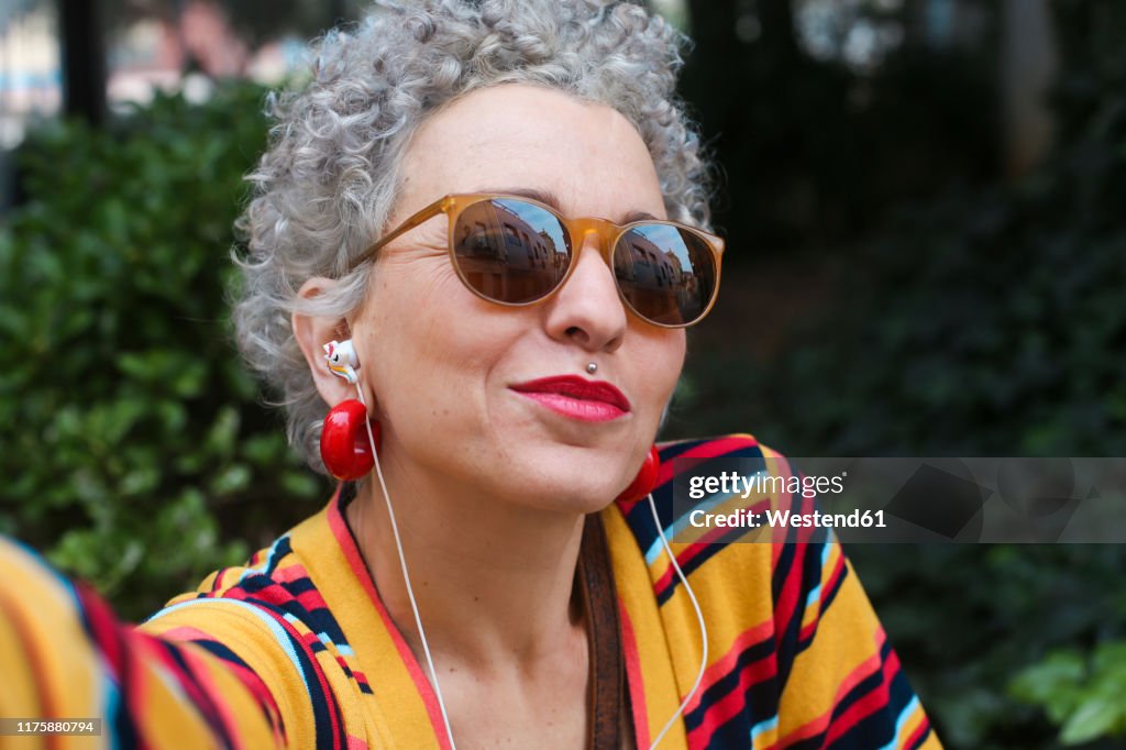 Portrait of pierced mature woman wearing sunglasses and earphones