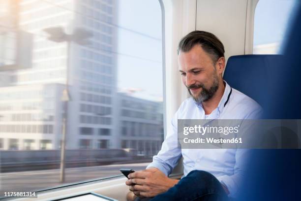 mature man sitting in a train, using smartphone - bart zug stock-fotos und bilder