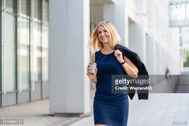 portrait of smiling blond businesswoman with coffee to go wearing blue summer dress - geschäftsfrau kleid stock-fotos und bilder