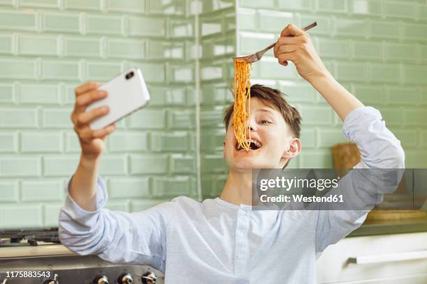 laughing boy taking smartphone selfie, eating spaghetti - teen boys selfie - fotografias e filmes do acervo