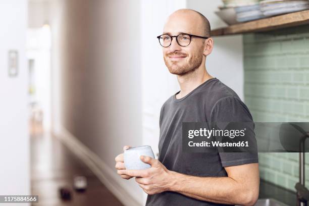 man with a cup standing in the morning at home in the kitchen - bald 30s stockfoto's en -beelden