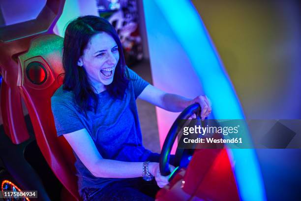 excited woman playing and having fun with a driving simulator in an amusement arcade - arcade stock pictures, royalty-free photos & images