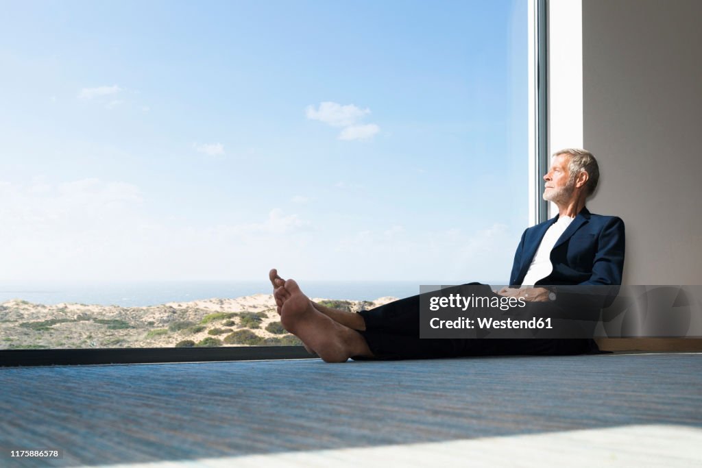 Senior businessman sitting at panorama window looking out