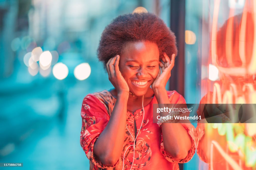 Smiling young woman with headphones standing next to neon light