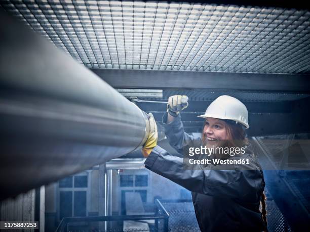 happy craftswoman wearing hard hat working at pipe - pipe women stock pictures, royalty-free photos & images
