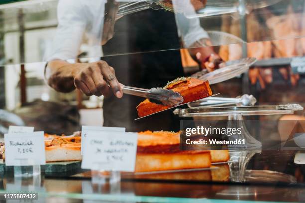man working in a bakery putting a piece of cake on a plate - cake sale stock-fotos und bilder