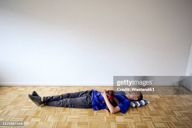 young man laying on the floor in an empty apartment embracing a teddy bear - bear lying down stock pictures, royalty-free photos & images