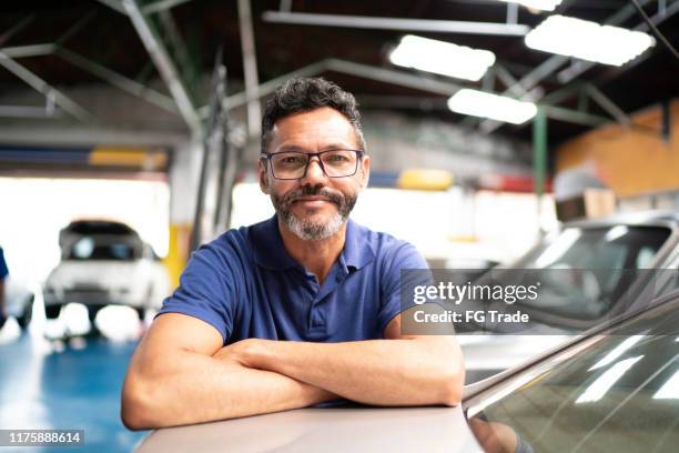 ritratto di un uomo con le braccia incrociate appoggiate in un'officina di riparazione auto su un'auto - auto entrepreneur foto e immagini stock