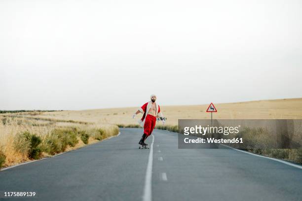 santa claus riding on longboard on country road - claus lange stock pictures, royalty-free photos & images