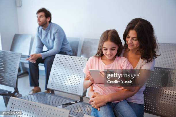 smiling girl using digital tablet on mother's lap - hospital waiting room stock pictures, royalty-free photos & images