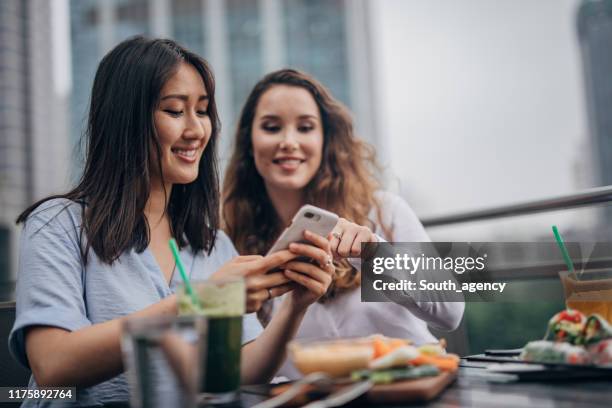 ladies using phone outdoors in restaurant - restaurant women friends lunch stock pictures, royalty-free photos & images