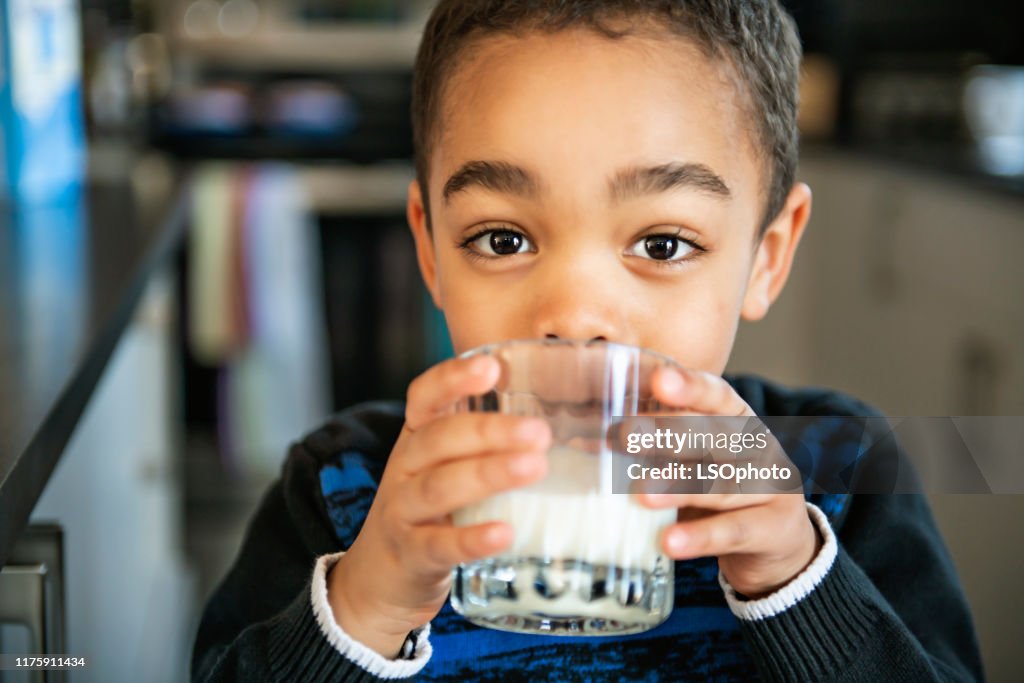 Cute African American boy drinking milk at home