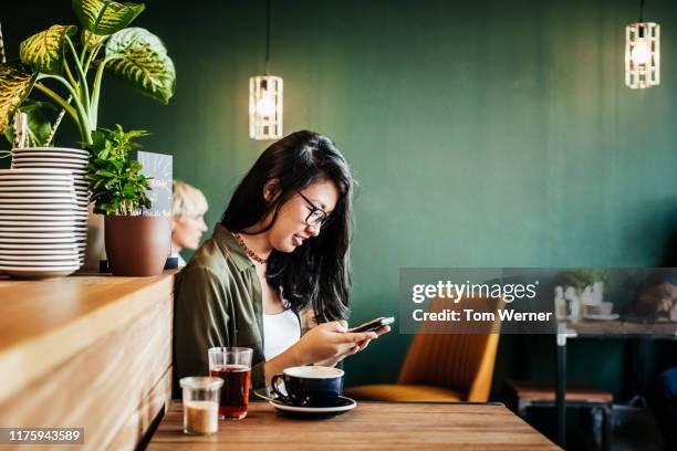 young woman sitting in cafe using smartphone - green shirt stock pictures, royalty-free photos & images