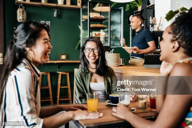 three friends laughing at chatting in coffee shop - female with friend in coffee stock pictures, royalty-free photos & images