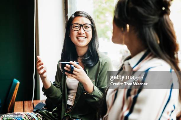 two friends catching up over coffee in cafe - asian woman coffee stock-fotos und bilder