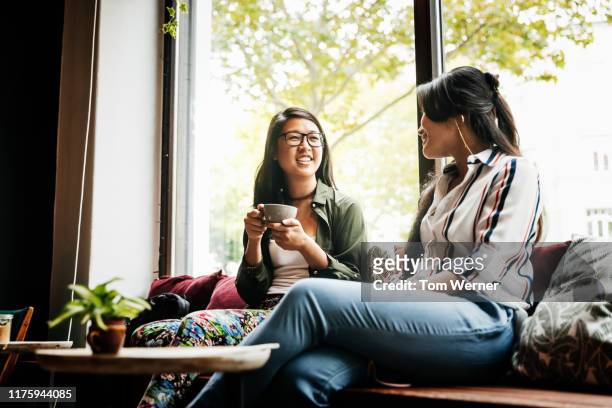two friends sitting in favorite cafe drinking coffee - asian friends coffee stock-fotos und bilder