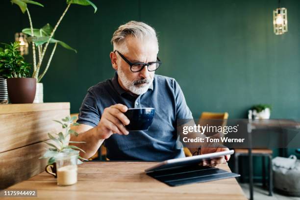 mature man sitting in cafe reading on tablet - blue polo shirt photos et images de collection