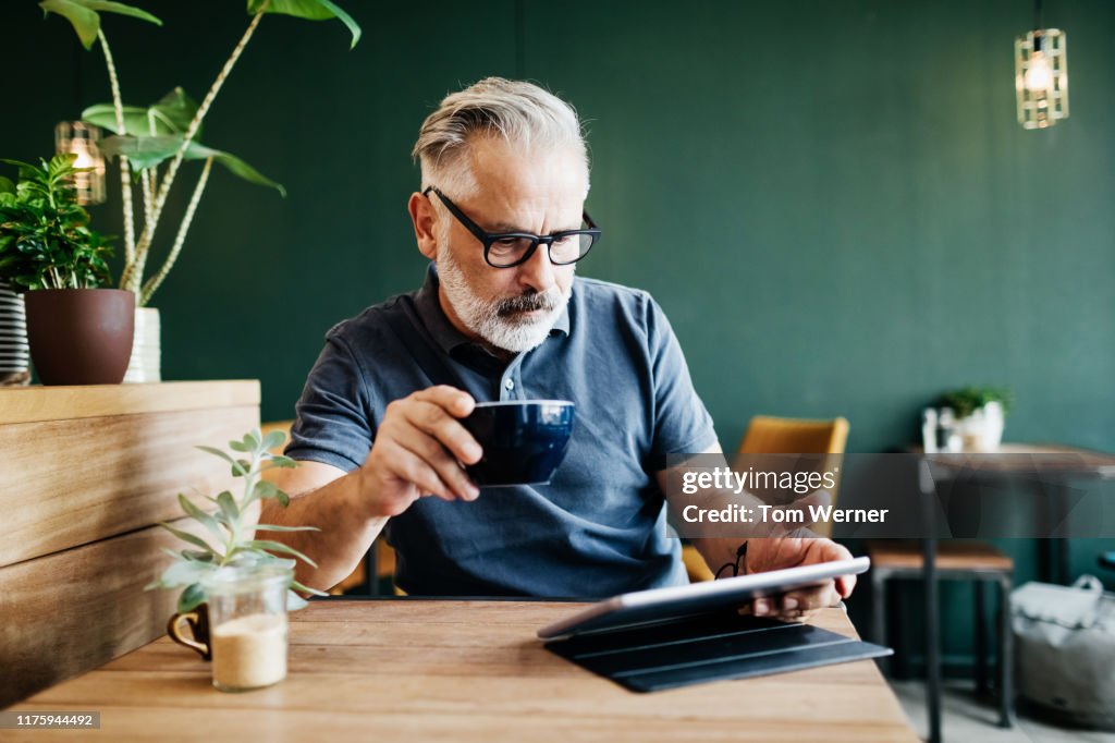 Mature Man Sitting In Cafe Reading On Tablet